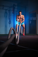 Fototapeta na wymiar Muscular fitness man working out with battle ropes