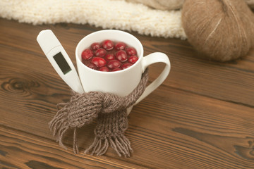 Cup of tea with cranberries, scarf, thermometer - the concept of seasonal respiratory diseases, treatment of colds