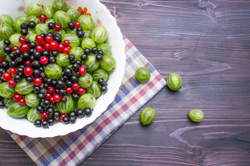 Green gooseberry, red and black currants on a wooden background.View from above.