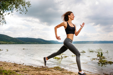 A beautiful sporty woman runing on the shore of a lake in sportswear. Girl is exercising