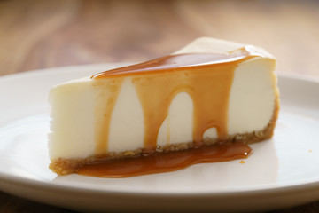 caramel sauce poured on slice of traditional new york cheesecake on white plate on wood table