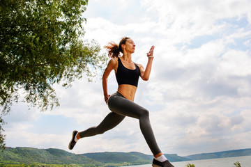 Fototapeta na wymiar A beautiful sporty woman runing on the shore of a lake in sportswear. Girl is exercising