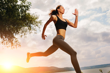 A beautiful sporty woman runing on the shore of a lake in sportswear. Girl is exercising