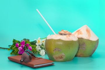 coconut with drinking straw, notebook and sunglasses on blue background