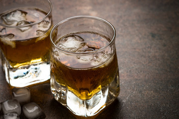 Whiskey with ice in glass on dark stone table.