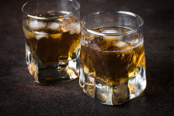 Whiskey with ice in glass on dark stone table.