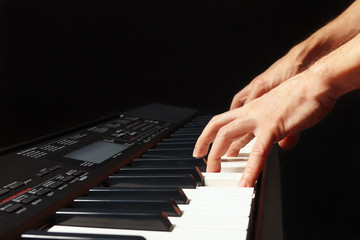 Hands of musician playing the electronic piano on a black background