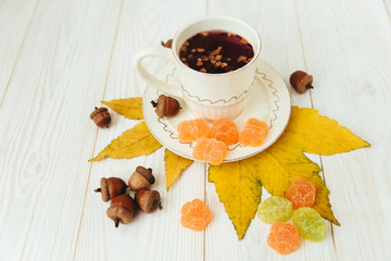 Cup of fruit tee with autumn elements on the white wood.Jelly candy,leaves,acorns.