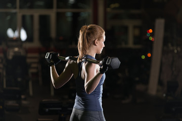 Beautiful sporty woman doing power fitness exercise at sport gym. Girl with dumbbell on black.