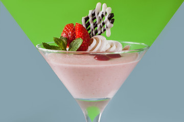 Creamy strawberry dessert on contrast v-shaped grey and green background. Sweet fruit souffle decorated with fresh red berry, chocolate and mint, close up picture