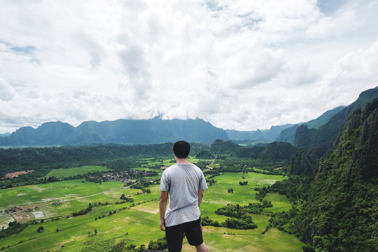 a man standing on mountain peak, traveling in tropical countryside, Vang Vieng in Laos