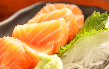 Japanese food: salmon sashimi (fresh raw salmon meat) decorated with grated turnip and mint leaf on wooden table as a background.