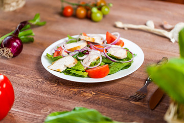 Fresh salad with chicken, tomato and greens on wooden background top view. Healthy food.