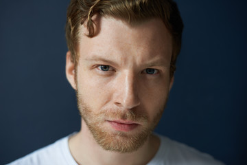 Fototapeta premium Highly-detailed close up portrait of attractive confident young European male with beard and beautiful blue eyes frowning, having serious thoughtful look. Human facial expressions and emotions