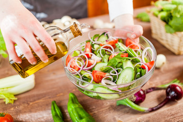 man pouring olive oil into healthy salad on kitchen