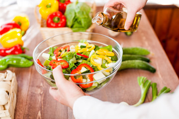 man pouring olive oil into healthy salad on kitchen