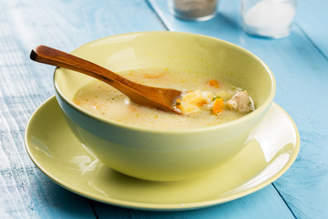 Green bowl filled with soup with vegetables and meat on the blue table