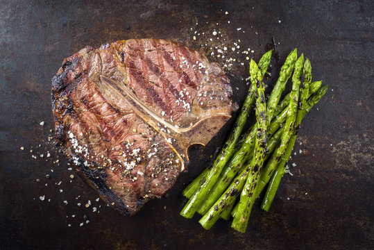 Barbecue dry aged Wagyu Porterhouse Steak with green Asparagus as close-up on an rusty board