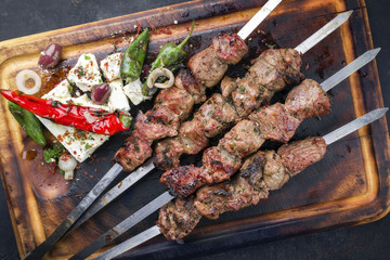 Traditional Greek Souvlaki with Feta and Vegetable as top view on an old burnt cutting board