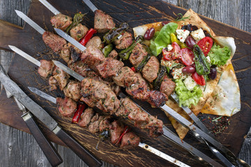 Traditional shashlik with salad and yufka bread as top view on an old burnt cutting board
