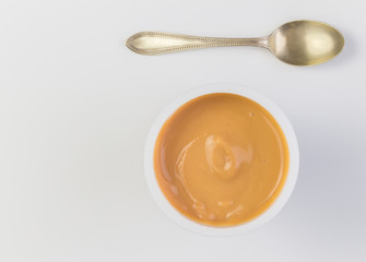 Yogurt background top view shot of caramel flavoured yoghurt in plastic cup with small silver spoon isolated on white background - close up image with space for text