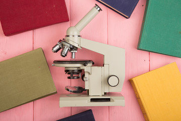 Education concept - microscope and colorful books on the yellow wooden desk