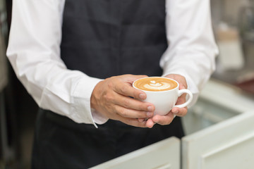 Barista holding cup of heart latte art coffee in coffee shop.