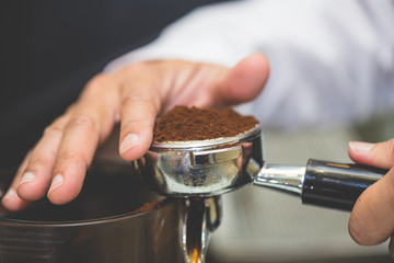 Hand of barista using tamper to press ground coffee into portafilter in cafe for prepare to make espresso coffee.