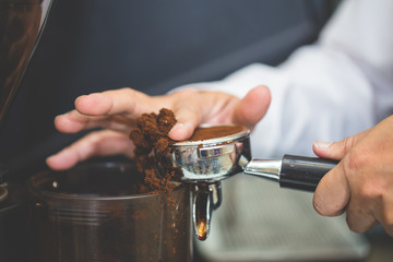 Hand of barista using tamper to press ground coffee into portafilter in cafe for prepare to make espresso coffee.