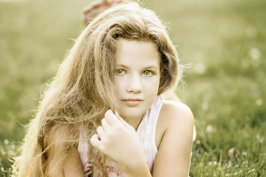 A teenage girl touching long hair and lying on grass in summer