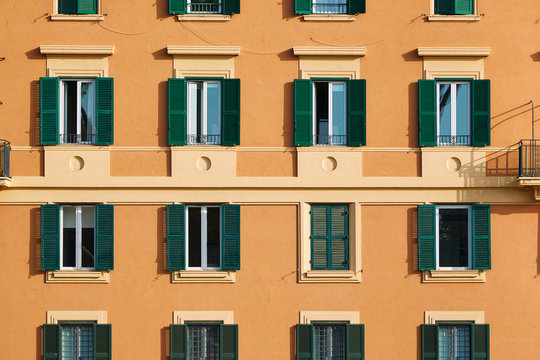 Part of the facade of an orange italian  building with windows with green shutters
