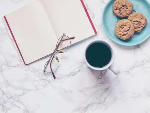 Black coffee and open notebook or journal with glasses and crunchy chocolate chip cookies or biscuits on a decorative plate on marble background. Flat lay. Top view. Copy space