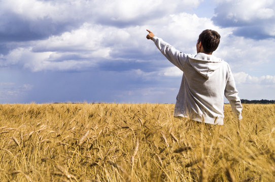 Man in a wheat field showing his fingers in the direction of the sky
