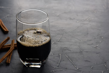 Cup of cold coffee on dark background. Iced espresso in a glass with cinnamon sticks on grey stone table. Copy space