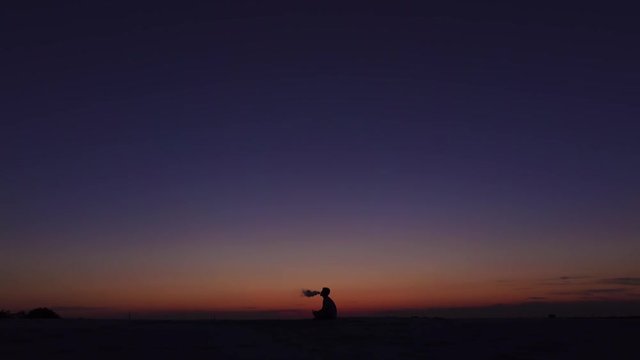 Guy smokes an electronic cigarette against the sunset with his relax. Silhouette