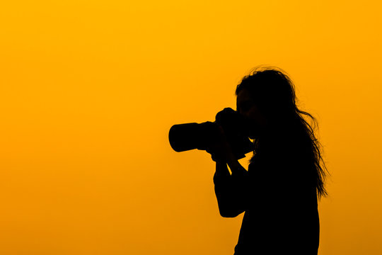 Silhouette of a girl  photographer with DSLR camera and tele lens at sunset on rooftop. Photographer life concept.