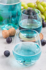 Trendy blue moscato wine in glass and in bottle, green and red grape on background, vertical