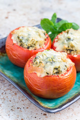 Baked tomatoes stuffed with quinoa and spinach topped with melted cheese on the plate, vertical, copy space