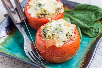 Homemade baked tomatoes stuffed with quinoa and spinach topped with melted cheese on the plate, horizontal