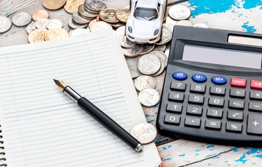Notepad with calculator, coins and car model on the table.