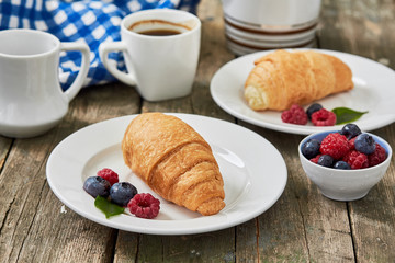 Morning breakfast with cup of coffee, croissants and fresh berries on old wooden background