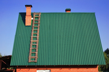 Green metal roof on the house, with a brick pipe and a wooden staircase