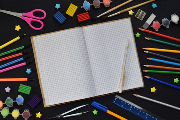 School accessories and supplies: pencils, markers, paints, pens, blackboard for inscriptions on a dark background. Back to school. View from above. Flat lay