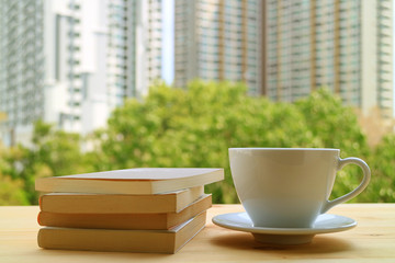 Relaxing with a cup of hot drink and some books by the window, with Blurred Background of green trees and high buildings 