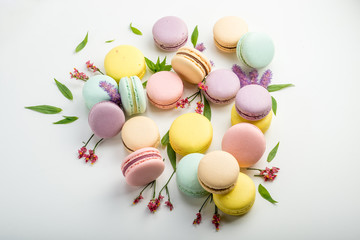 Fototapeta na wymiar Colorful macarons with leaves and red flowers on a white background. French delicate dessert