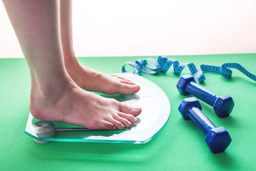 Female feet standing on electronic scales, dumbbells and measuring tape. Concept of slimming and weight loss