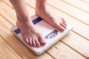 Female feet standing on mechanical scales for weight control on wooden background. Concept of slimming and weight loss