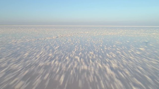 Low angle drone fast flying forward over the white salt lake with deposits of salt. Aerial view.