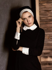 Humble young beautiful nun in robes holding a cross on a grey background