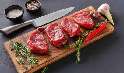 Filet mignon steaks and spices on wood at black background